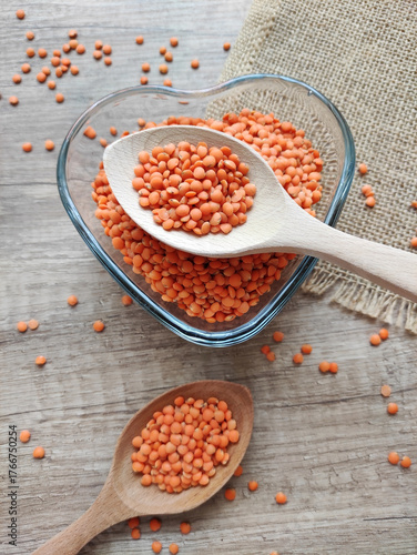 Dried small red lentils in a decorative plate and wooden spoons on a wooden background	