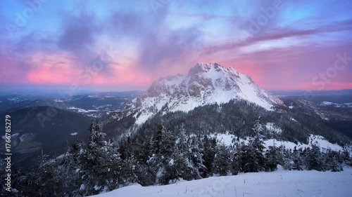 Winter mountain peak at sunrise with colorful pink and blue sky above snowy forest and valley