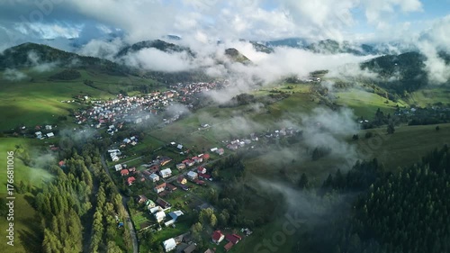 Aerial hyperlapse of mountain village with drifting fog and morning sunlight over green valley