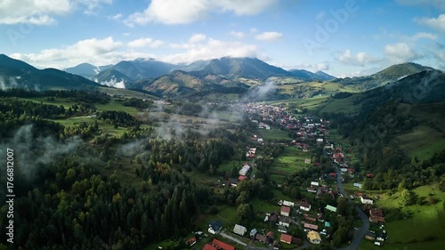 Aerial hyperlapse of mountain village with drifting fog and morning sunlight over green valley