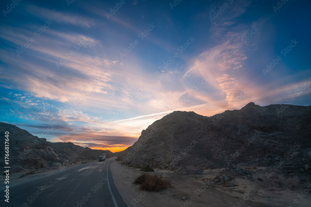 Fototapeta premium Spring dusk in Hurghada, Egypt, reveals dramatic clouds, rocky hills, and roadside power towers during a scenic bus ride.