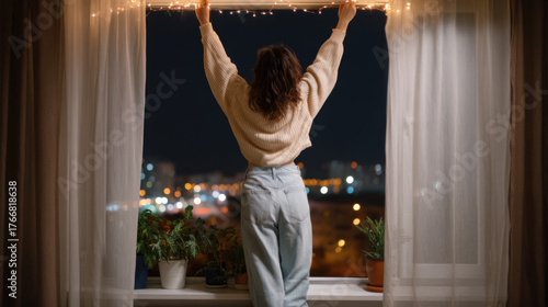 Woman decorating house with festive holiday lights from window during Christmas and New Year celebration