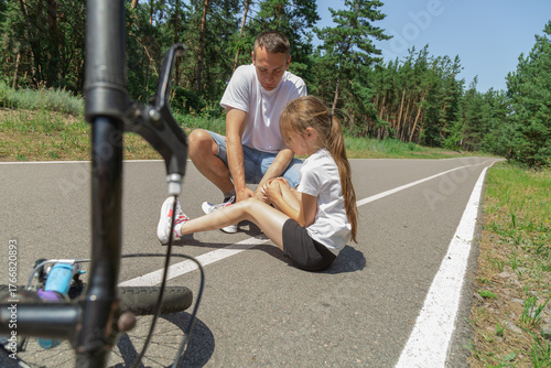Father helping her little daughter after falling off bicycle in forest
