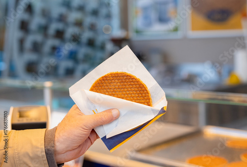 Tourist hand holding Traditional Dutch fresh made Stroopwafel, Street food treat made from thin, crispy waffles filled with rich caramel syrup, freshly prepared at local markets in The Netherlands. 