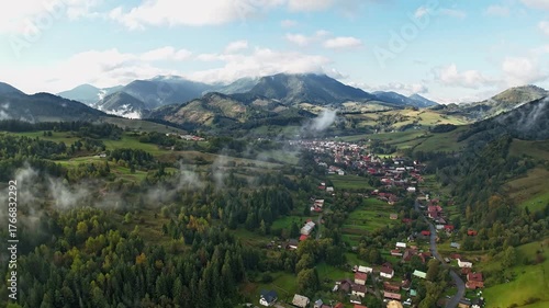 Aerial hyperlapse of mountain village with drifting fog and morning sunlight over green valley