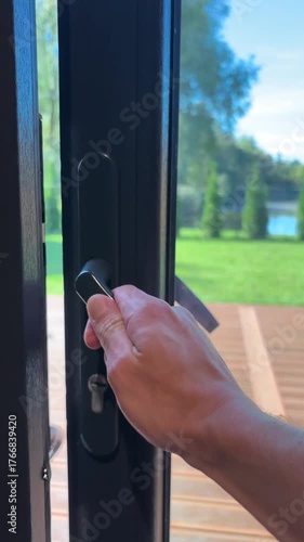 Man opens the door of a house and looks out onto a yard with green grass, trees and a lake.