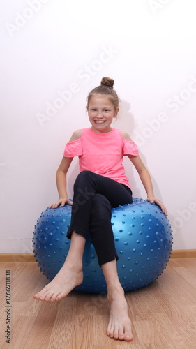A happy smiling girl sitting on a balance ball, enjoying exercise and playtime. Concept of childhood activity, balance, coordination, and fun fitness.