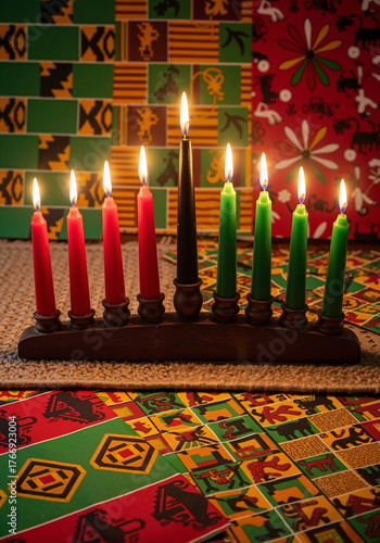Kwanzaa candles lit on wooden holder with colorful patterned background  