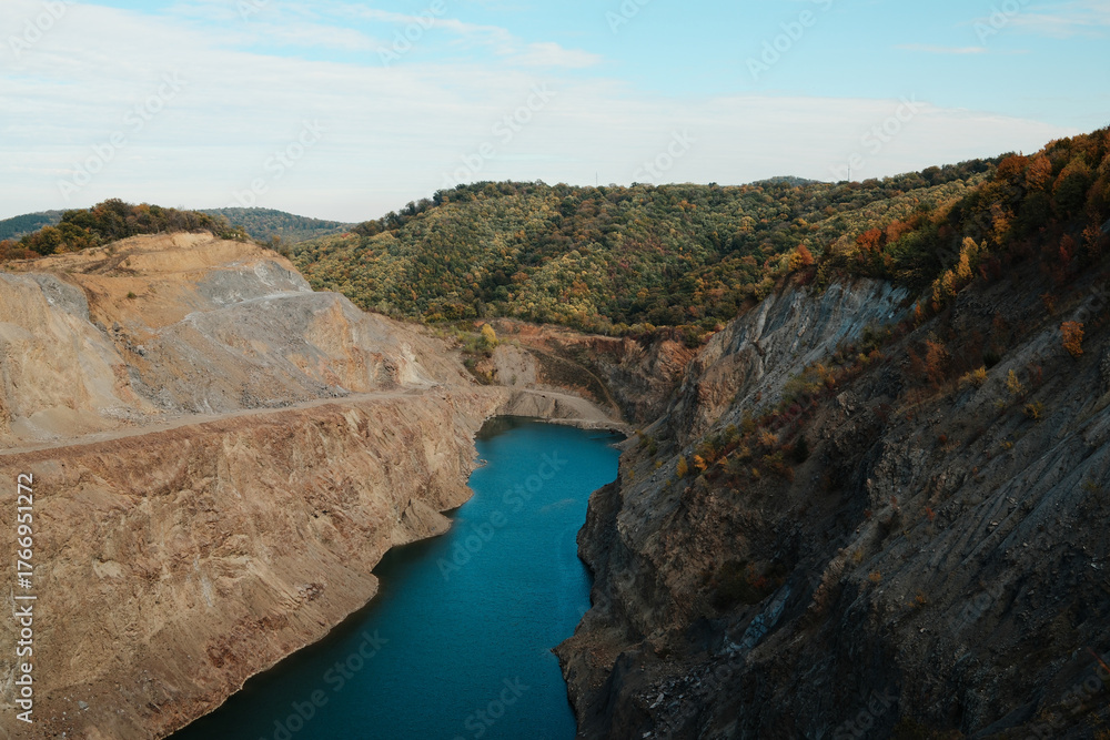 Fototapeta premium Scenic view of blue water lake in rocky quarry surrounded by colorful autumn forest and hills in Fruska Gora Serbia