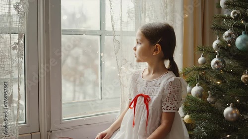 Turbo young girl sitting quietly by a window, gazing outside with a thoughtful expression, cozy Christmas atmosphere, soft natural window light, decorated Christmas tree with glowing fairy light