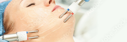 Papier peint Caucasian female receiving facial electrostimulation treatment with conductive gel in spa setting