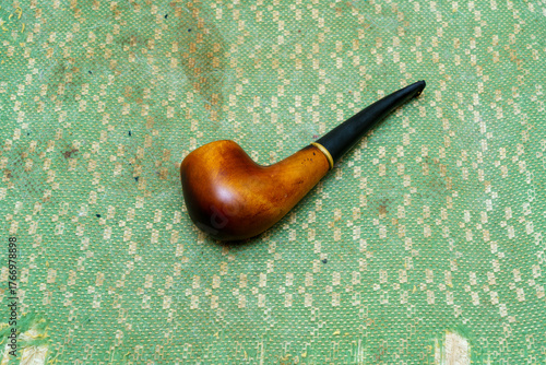 Elegant wooden smoking pipe resting on a textured green surface indoors