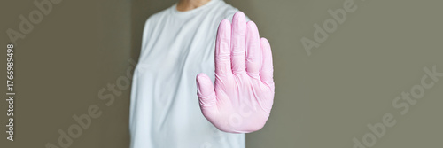 Caucasian female adult with raised hand wearing pink gloves and white t-shirt demonstrating stop gesture.