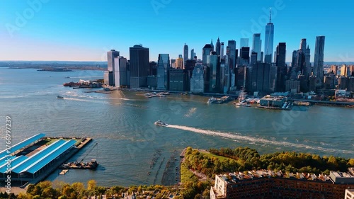 Descending over Brooklyn on sunny day. Boat moves by the East River. Iconic skyline of Manhattan at backdrop.