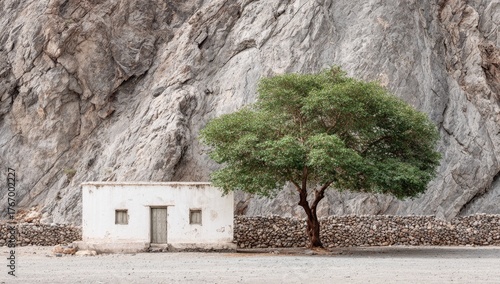 A whitewashed hut nestled against a craggy mountainside, with a solitary tree