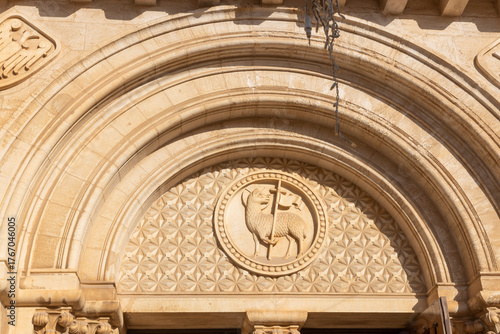 Close-up of a romanesque stone archway featuring a carving of the lamb of god, set against a geometric background pattern.  Lutheran Church of the Redeemer in Jerusalem, Israel