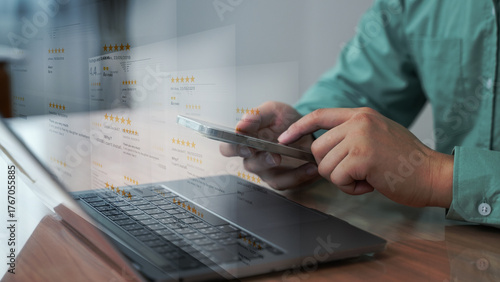 Close-up of a person browsing customer reviews and star ratings on a smartphone with a laptop on a desk, indicating e-commerce research.
