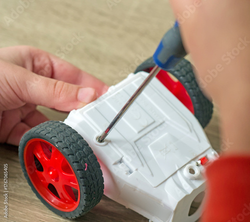 Photography A person's hands use a tool to unscrew the battery cover on a white toy car - Cl