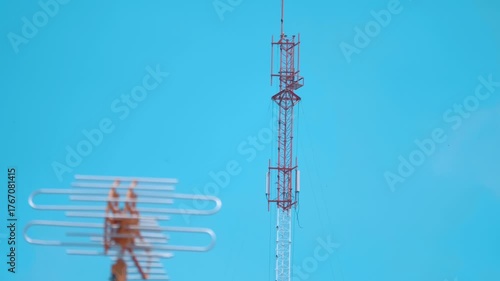 A TV antenna is catching the signal of a nearby telecommunication tower against the background of a blue sky