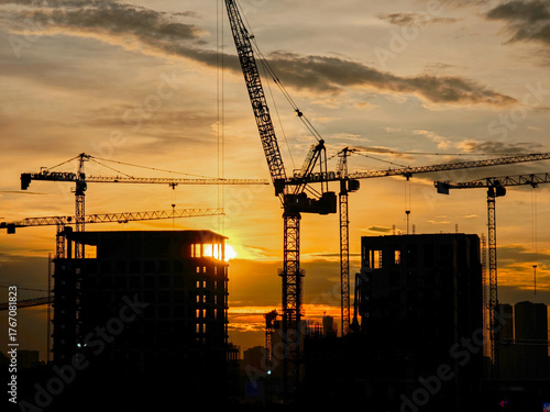 Construction site and tower cranes against the backdrop of a bright sunset