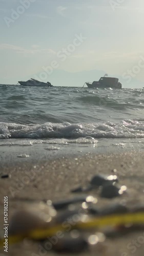Foamy sea waves wash the sandy shore. Fishing boats in the sea  in the background. Aegean Sea in Greece, Halkidiki.