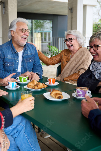 Vertical. Happy group senior people laughing, enjoying coffee sitting at cafeteria bar. Retired generation community friends having fun gathered on terrace eating breakfast and drinking hot beverage