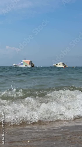 Slow motion as sea waves crash against the sandy shore. Fishing boats sway on the waves in the Aegean  Sea bay. Seaside vacation. The coast of the Aegean Sea in Greece, Halkidiki. Relaxing