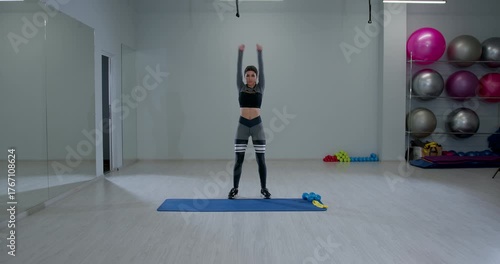 athletic woman is doing arm circles in a spacious fitness studio showcasing her strength and coordination. The workout area is well lit and inviting filled with exercise equipment.