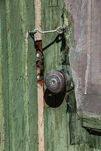 An old green painted door is latched closed with a hook.