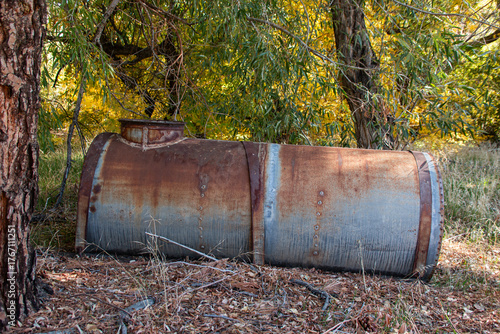 An old galvanized metal tank used for water storage near an abandoned residence in the woods.