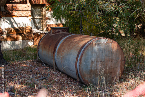 An old galvanized metal tank used for water storage near an abandoned cabin in the woods.