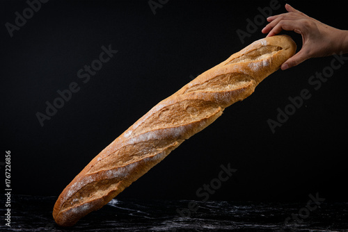 A hand proudly presents a long, golden-crusted French baguette