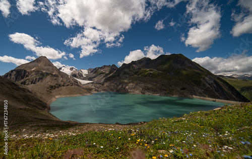 Turquoise Gries Lake and glacier near Corno-Gries Pass in the Swiss Alps. Stunning alpine landscape with rugged peaks, hiking trails, and wildflowers under a bright summer sky.