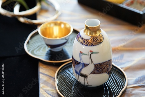 A sake set, consisting of an ochoko cup and tokkuri flask, used for drinking Japanese sake an alcoholic beverage, which is decorated with a crane design and gold coloring