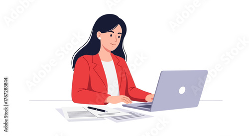 Professional businesswoman in a red jacket working on a laptop computer at her office desk with documents.