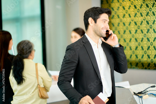 A businessman with casual black suit talking with mobile phone after check in complete at airport counter for travel by airplane to business trip.