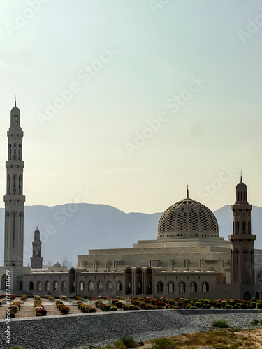 Grand Mosque in Muscat, Oman at sunrise, Scenic view of a mosque surrounded by mountains in Muscat, Oman, captured during the golden morning light.

