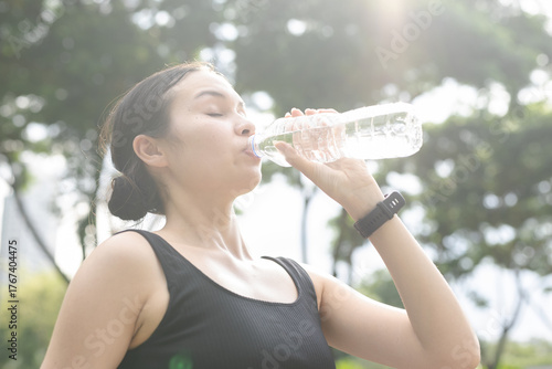 women drinking water from plastic bottle outdoors on sunny day, staying hydrated after exercise. Concept for healthy lifestyle, hydration, summer heat and fitness recovery.