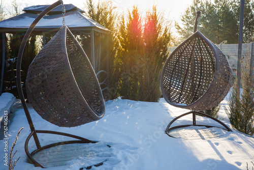 Hanging cocoon chair, rattan garden swing. View of the relaxation area near the house during the winter and frosty period.