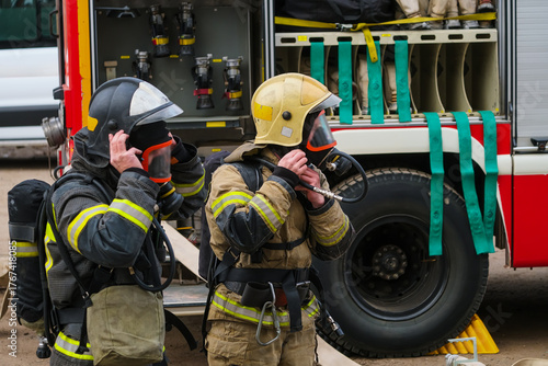 Firefighters in protective suits and masks with breathing apparatus, against the background of a fire truck.