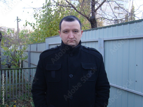 portrait of a young man. man in a coat.Casual portrait of a man standing outdoors near a fence on an autumn day. Natural light