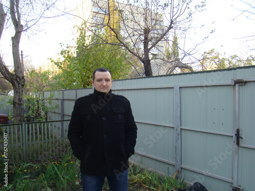 portrait of a young man. man in a coat.Casual portrait of a man standing outdoors near a fence on an autumn day. Natural light