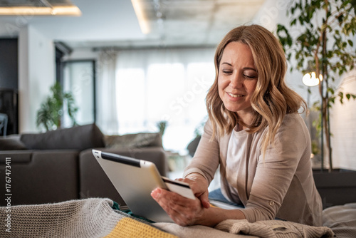 Smiling woman using digital tablet and credit card for online shopping at home