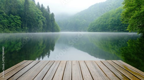 Serene morning mist over calm water surface reflects lush green trees