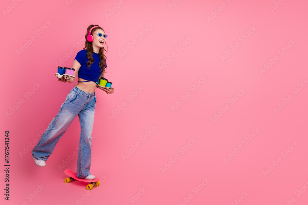 Obraz premium Young woman roller skating on pink background holding colorful beverages, wearing trendy outfit and smiling confidently