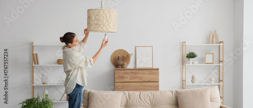 Young woman screwing light bulb into stylish lamp in living room