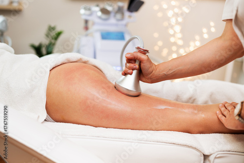 Professional beautician using a specialized device, performing an anti-cellulite treatment on a woman's thigh in a modern spa or beauty salon, ensuring smooth and toned skin