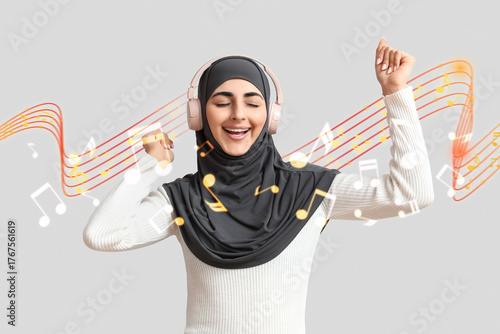 Happy Muslim woman with headphones listening music on grey background