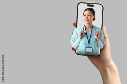 Patient holding smartphone with female Asian doctor looking out of screen aga...