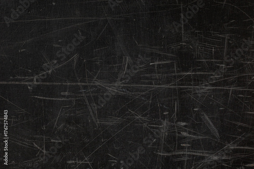Dark, heavily scratched surface, worn chalkboard or a painted metal sheet, covered with a dense, chaotic pattern of thin, light-colored scuff marks and abrasions, gritty, textured, grunge abstract bac